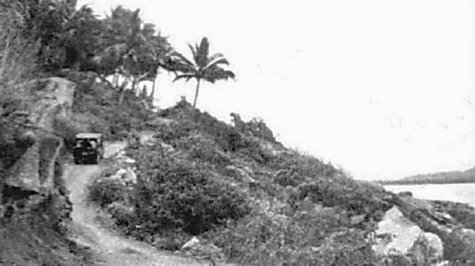 An old black and white photo of a car driving down a hill.