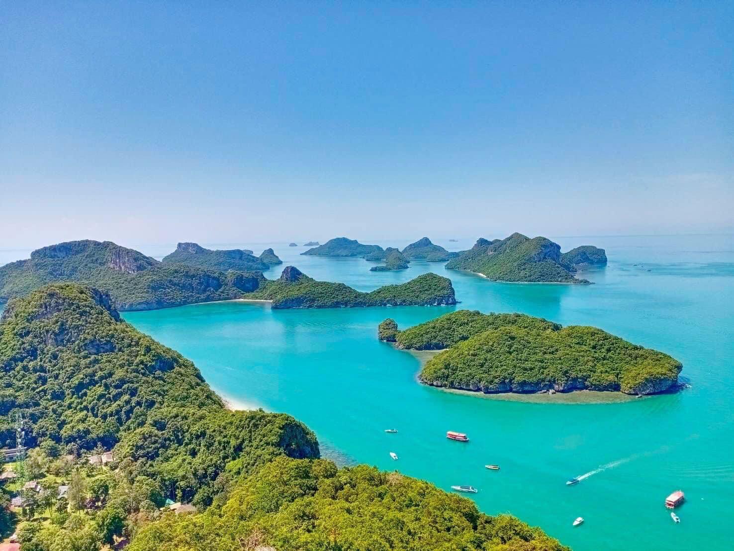 Aerial view of a tropical archipelago with emerald waters, lush green islands, and boats dotting the coastline.