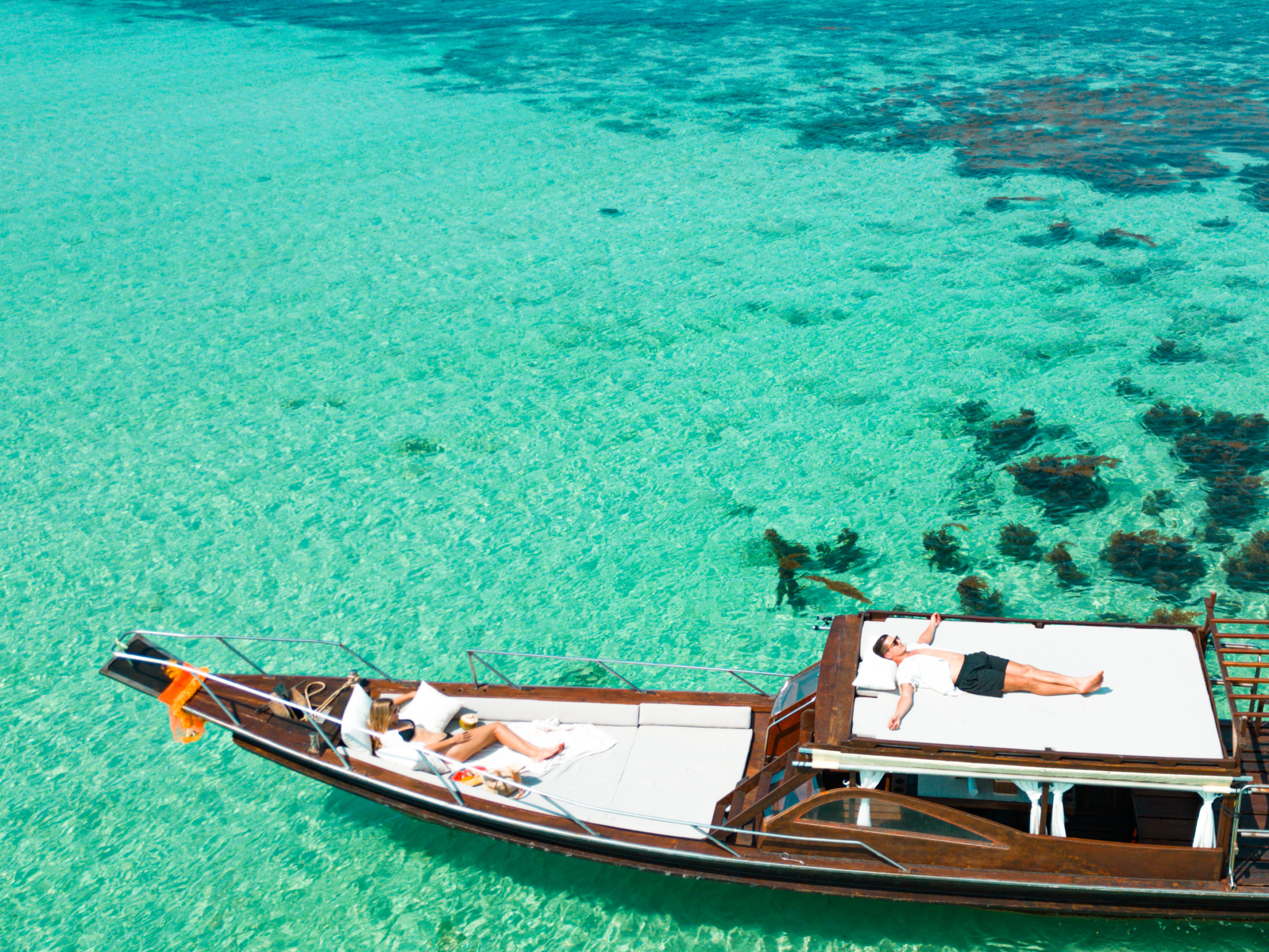A person relaxing on the bow of a wooden boat over clear turquoise waters.